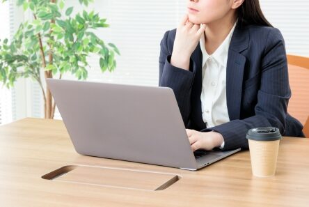 ノートパソコンを前に考え込む女性の写真。委託先選びを検討するイメージ
