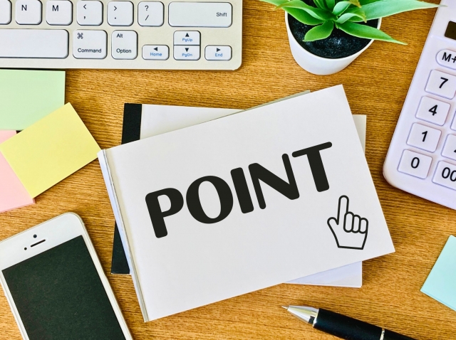 「POINT」と書かれたメモ帳と文房具、観葉植物が置かれたデスクの写真